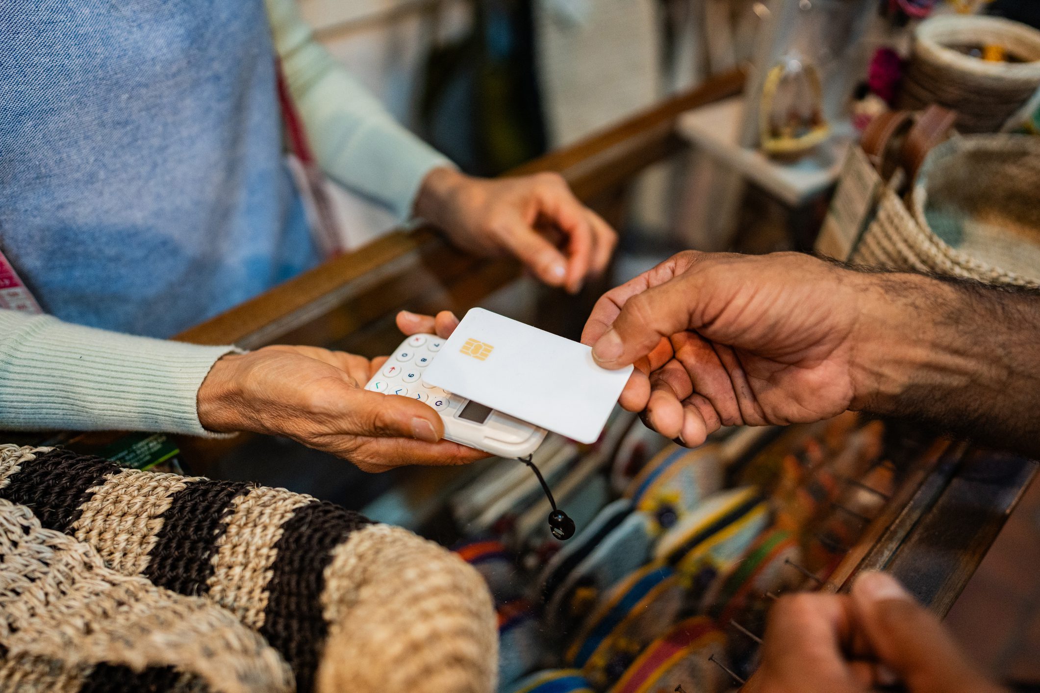 Close-up of hands exchanging a card over a market stall with woven goods.